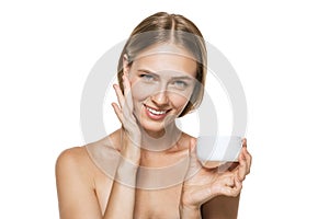 Beauty portrait of happy smiling beautiful half naked girl applying face cream and looking at camera isolated over white