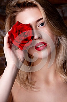 Beauty portrait of lovely girl with red lips posing at studio with red rose at her eye