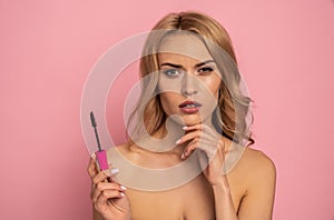 Beauty portrait of a lovely young woman with long blonde hair standing isolated over pink background, showing eye mascara