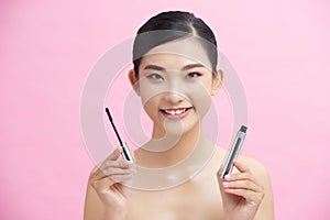 Beauty portrait of a lovely young woman standing isolated over pink background, showing eye mascara