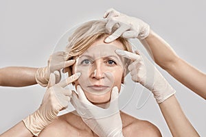 Beauty portrait of middle aged woman going under cosmetic treatment. Beautician hands in gloves checking female face