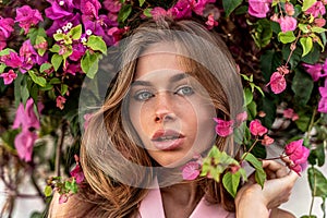 Beauty portrait of natural young attractive woman with freckles on her face posing in pink bush of flowers