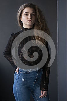 Beauty portrait of a pretty young woman, dressed in a black suitcase and jeans, over grey background.