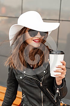 Beauty portrait smiling woman with cup of  coffee with red lips in vintage hat in black fashion jacket in cool sunglasses near