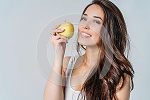 Beauty portrait of smiling young asian woman girl holding green apple near clean face on grey background