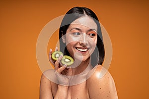 Beauty portrait of smiling young woman with natural freckles. Girl holding organic kiwi in hand. Skin care concept