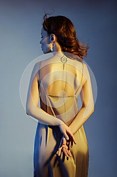 Beauty portrait of a woman with earrings and golden chain on neck back. Expensive jewelry