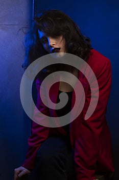 Beauty portrait of woman with makeup and hairstyle, wear red suit, looking at camera, over blue neon studio light.