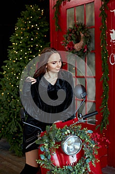 Beauty portrait of a woman on a red scooter moped, Christmas interior. A woman with long beautiful hair in a black dress, natural