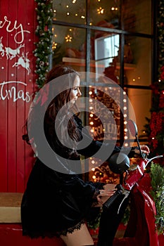 Beauty portrait of a woman on a red scooter moped, Christmas interior. A woman with long beautiful hair in a black dress, natural