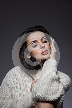Beauty portrait of woman in white sweater, perfect evening makeup on dark background. Perfect skin without wrinkles, professional