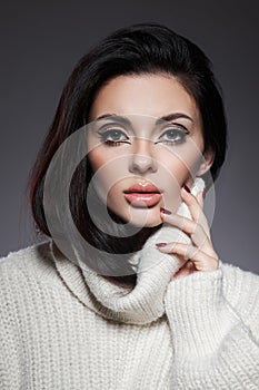 Beauty portrait of woman in white sweater, perfect evening makeup on dark background. Perfect skin without wrinkles, professional