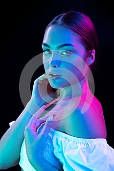 Beauty portrait of young adorable woman with well-kept skin isolated over dark background in purple neon light. Concept