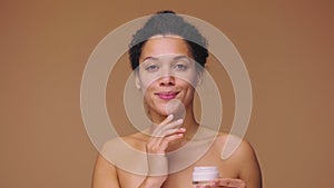 Beauty portrait of young African American woman applying skincare cream on face. Healthy skin care face. Black female