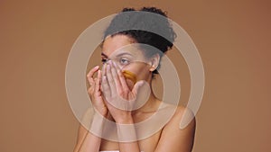 Beauty portrait young African American woman applying skincare scrub on face, rubbing gently with fingers. Black female