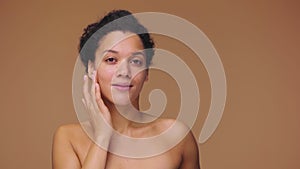 Beauty portrait young African American woman applying skincare serum on face, rubbing gently with fingers. Black female