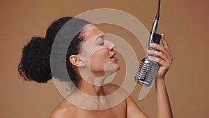 Beauty portrait of young African American woman singing song into vintage retro microphone. Black female model posing on