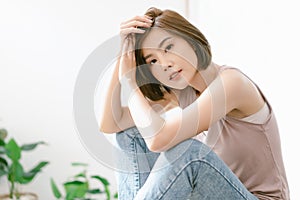 Beauty portrait of young Asian woman with perfect fresh clean skin resting at home while sitting on table and looking at camera.