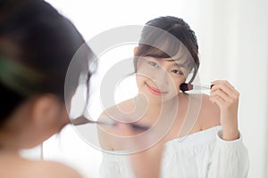 Beauty portrait young asian woman smile with face looking mirror applying makeup with brush cheek in the bedroom