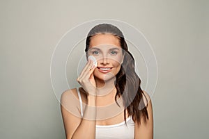 Beauty portrait of a young attractive woman cleaning her face with a cotton pad on white background