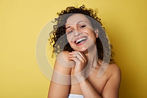 Beauty portrait of young half naked woman with curly hair smiling toothy smile looking at camera, posing over yellow background