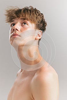 Beauty portrait of young man, teen looking up isolated on grey studio background. Concept of teenage skin care, health