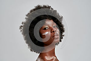 Beauty portrait of young naked african american woman with afro hair looking at camera while posing with cream applied
