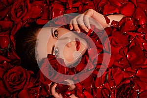 Beauty portrait, young woman in a bath with red rose petals, Top view, model with clean skin, retouching.