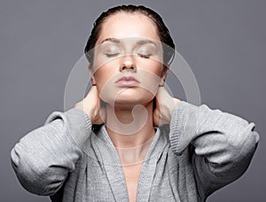 Beauty portrait of young woman in gray dress with hands on neck. Brunette girl with closed eyes and day female makeup