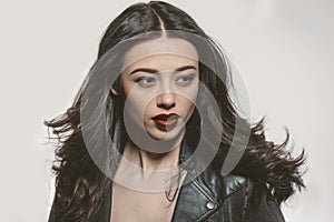 Beauty portrait of young woman in a leather jacket with beautiful long dark hair isolated on gray background. Young