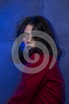 Beauty portrait of young woman with makeup and hairstyle, wear red suit, closed eyes, over blue neon studio light.