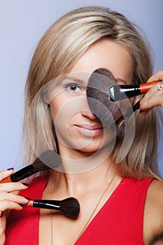 Beauty procedures, woman holds make-up brushes near face.