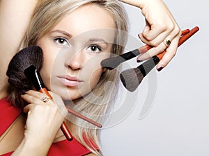 Beauty procedures, woman holds make-up brushes near face.