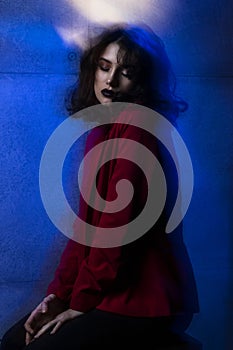 Beauty profile image of young woman with makeup and hairstyle, wear red suit, with closed eyes, blue neon studio light.