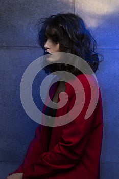 Beauty profile photo of young woman with makeup and hairstyle, wear red suit, with closed eyes, blue neon studio light.