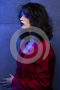 Beauty profile portrait of young woman with makeup and hairstyle, wear red suit, blue neon studio light.
