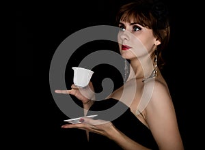 Beauty retro female model with professional makeup, drinking coffee or tea. fashion vintage woman on a dark background
