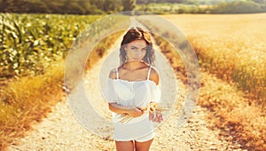 Beauty romantic girl enjoying nature in outdoors. Happy young woman in white shorts holding the ears of golden wheat