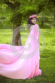 Beauty Romantic Girl Outdoors. Beautiful Teenage Model girl Dressed in blowing pink Dress on the Field at green park