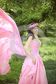 Beauty Romantic Girl Outdoors. Beautiful Teenage Model girl Dressed in blowing pink Dress on the Field at green park