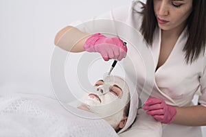 in beauty salon, facial care treatment nourishing face mask applied by beautician. close-up