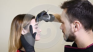 Beauty salon. Male beautician in black gloves applying eyebrow eyeliner before the permanent make-up procedure. Young