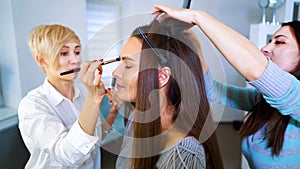 Beauty salon specialists doing professional makeup and hairstyle for young brunette woman