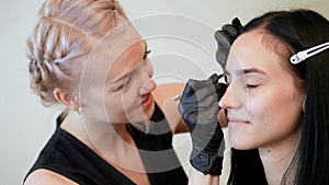 beauty saloon. the cosmetician in black rubber gloves hold tweezers and pull out eyebrows. Master corrects the shape of