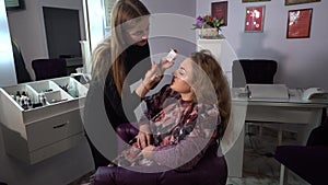 Beauty saloon. Young beautiful girl model is sitting in the chair. Makeup artist makes girl makeup. Blonde in a beauty