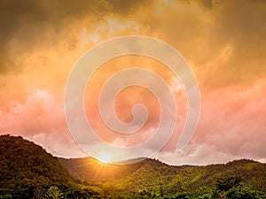 Beauty scenery of golden sunset cloudy sky with sun ray on the top of green mountain in the north of Thailand.
