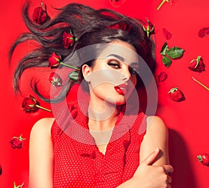 Beauty model girl lying on red background with rose flowers and strawberries. Beautiful brunette young woman with long hair
