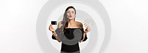 Beauty and shopping concept. Pretty glamour woman pucker lips for kiss, showing credit card and dollars, standing over