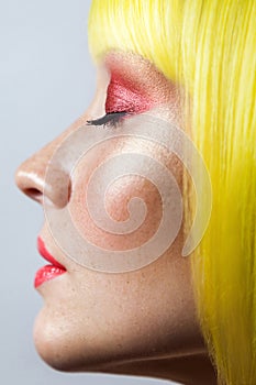 Beauty side view profile portrait of calm cute young female model with freckles, red makeup and yellow wig, closed eyes with