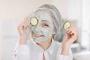 Beauty, skin care, antiwrinkle treatment concept. Headshot of beautiful Caucasian senior woman, holding cucumber piece